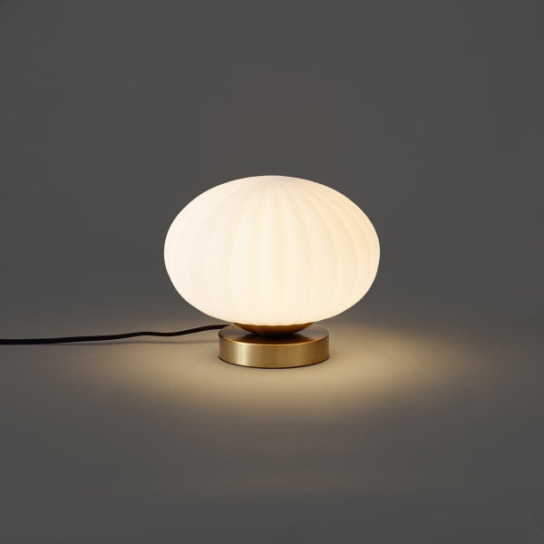 Tischleuchte mit geriffeltem Glasschirm und rundem Metallfuss in Messing-Optik, eingeschaltet.