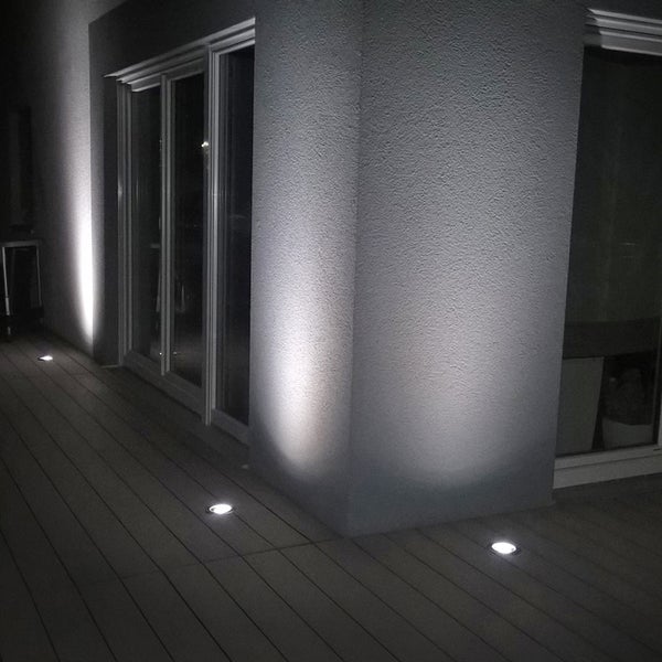 Bodeneinbaustrahler auf einer Terrasse beleuchten eine Hauswand bei Nacht.