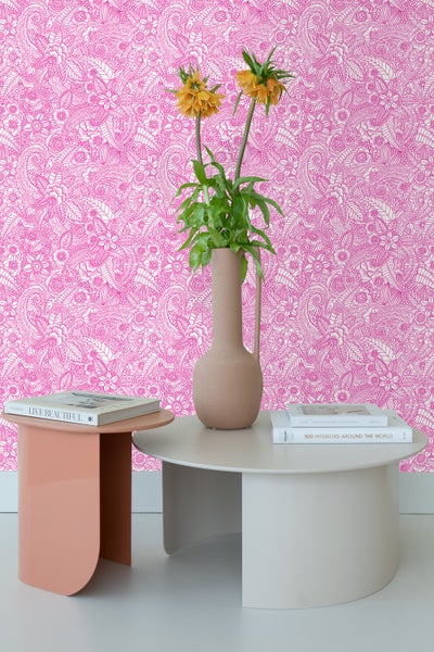Dekorative Tapete mit floralem Muster in Pink und Weiß hinter zwei Tischen mit Büchern und einer Vase mit Blumen.