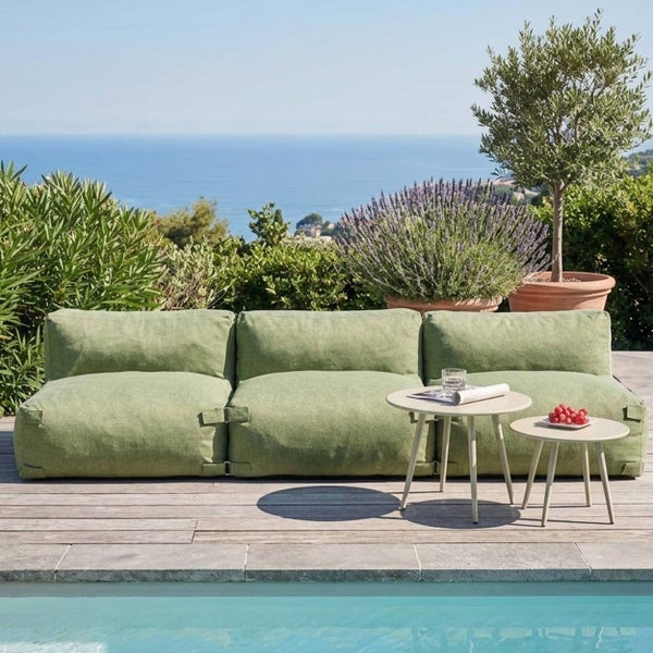 Grünes modulares Outdoor-Lounge-Sofa mit zwei runden Beistelltischen auf einer Holzterrasse am Pool mit Blick auf das Meer.