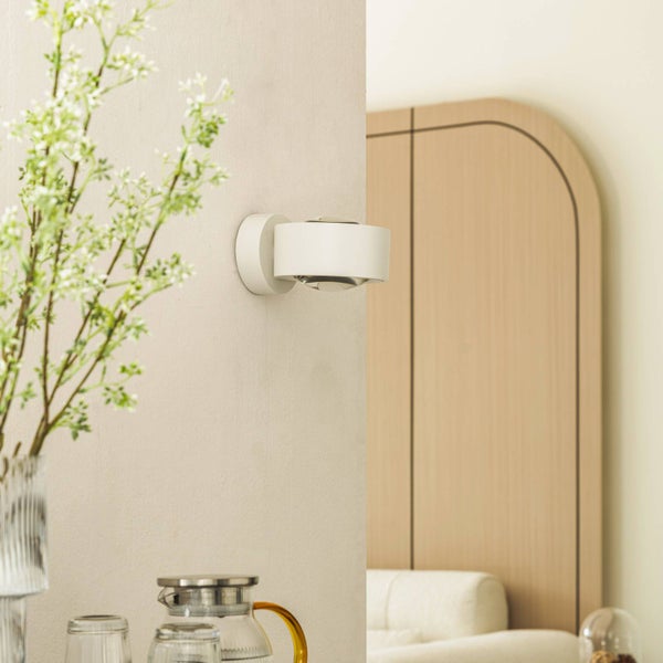 Moderne Wandleuchte an einer hellen Wand in einem hellen Zimmer mit einem Holzpaneel und Pflanzen.