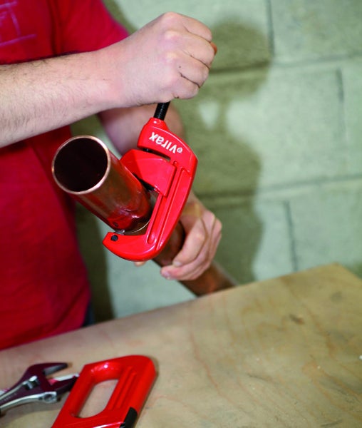 Ein Heimwerker nutzt einen roten Rohrabschneider mit Virax Logo an einem Kupferrohr.