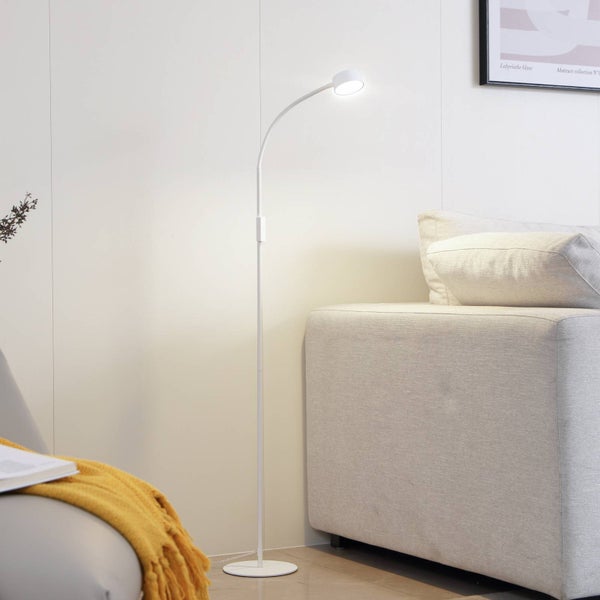 Moderne weiße Stehlampe mit flexiblem Arm in einem hellen Wohnzimmer neben einem Stoffsofa.