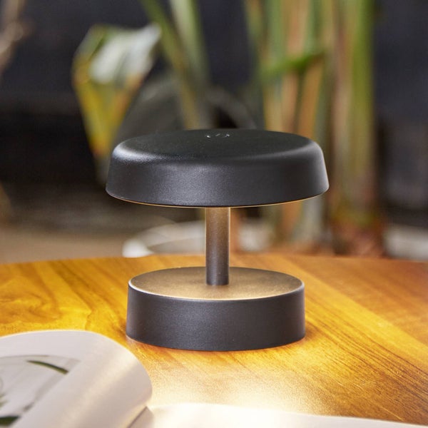 Kleine, kabellose LED-Tischleuchte in Schwarz auf einem Holztisch mit warmweißem Licht.