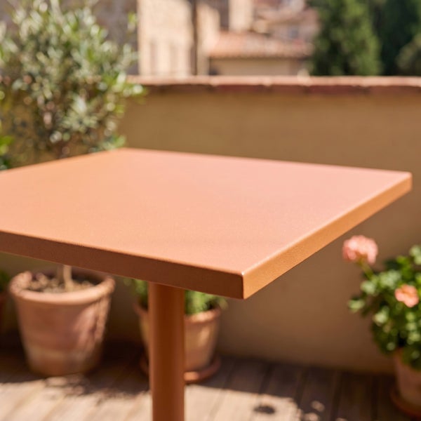 Quadratischer Gartentisch in Terrakotta auf einem Balkon mit Pflanzen, Detailansicht der Tischoberfläche.