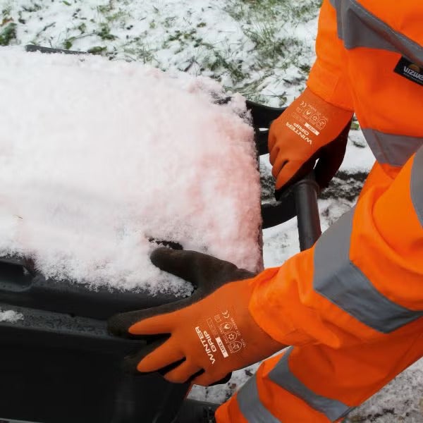 Person mit Winterhandschuhen beim Entleeren einer Schneeschaufel oder Mülltonne im Winter