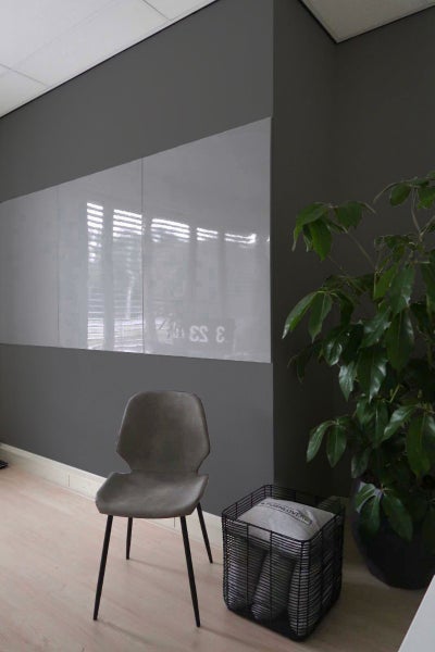 Drei rahmenlose Magnet-Glastafeln nebeneinander an der Wand montiert in einem modern eingerichteten Raum mit Stuhl und Pflanze.