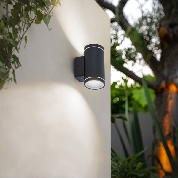 Schwarze, zylindrische Außenwandleuchte mit hellem Up-and-Down-Lichteffekt montiert an einer Wand im Garten.