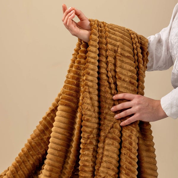 Weiche, gerippte Kuscheldecke in Cord-Optik, von Händen gehalten zur Veranschaulichung der Materialstruktur.