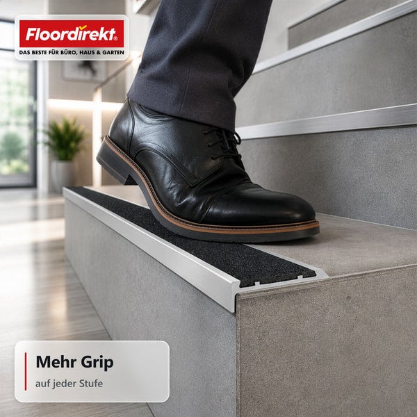 Person mit Lederschuh tritt auf eine Treppenkante mit rutschfestem Profil aus Metall und Kunststoff, Floordirekt Logo, mehr Grip auf jeder Stufe.