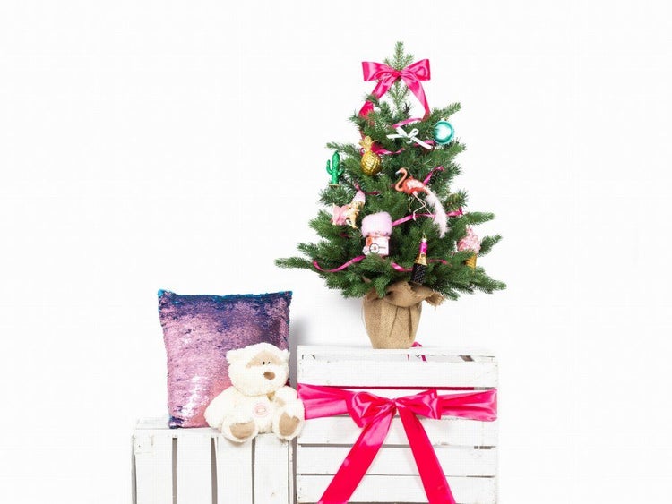 Geschmückter künstlicher Weihnachtsbaum in Jutesack auf weißen Holzkisten mit Teddybär und Paillettenkissen als Weihnachtsdekoration