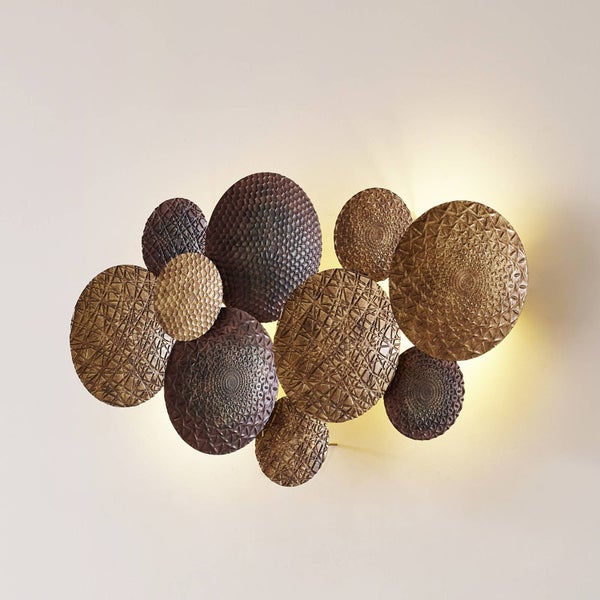 Wandleuchte aus überlappenden, strukturierten Metallscheiben mit indirekter Beleuchtung.