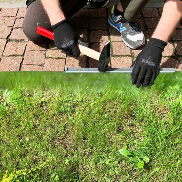 Person hämmert eine Metallschiene am Rasenrand mit einem Hammer ein.