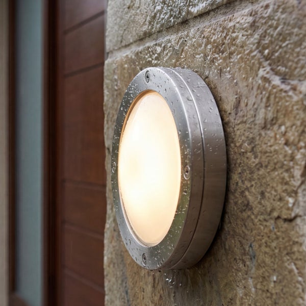 Runde Außenwandleuchte aus Metall mit matter Abdeckung, montiert an einer Steinwand, strahlt warmes Licht aus.