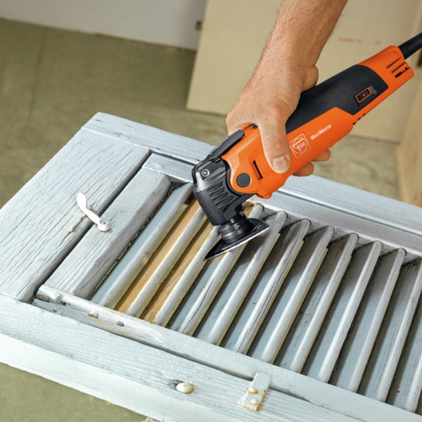 Eine Person verwendet ein Multifunktionswerkzeug, um Holz zu bearbeiten.