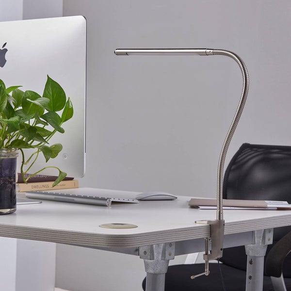 Moderne LED-Schreibtischleuchte mit flexiblem Arm und Klemme an einem weißen Tisch im Büro mit Computer und Pflanze.