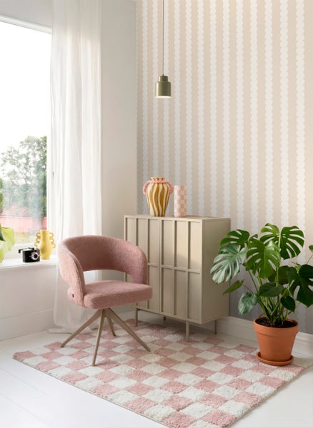 Heller Raum mit Tapete in Wellenoptik, rosa Polstersessel, beigem Sideboard, kariertem Teppich und einer großen Monstera-Pflanze.