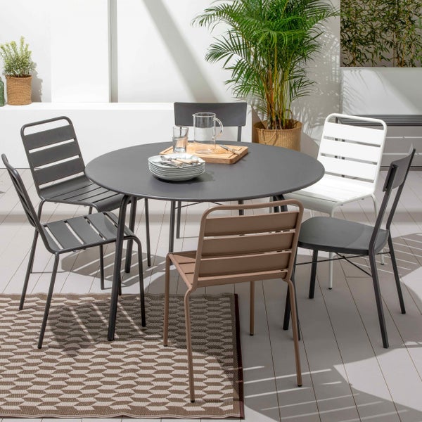 Moderner runder Gartentisch aus Metall mit passenden Metallstühlen auf einer hellen, organisierten Terrasse mit Teppich und Pflanzen.