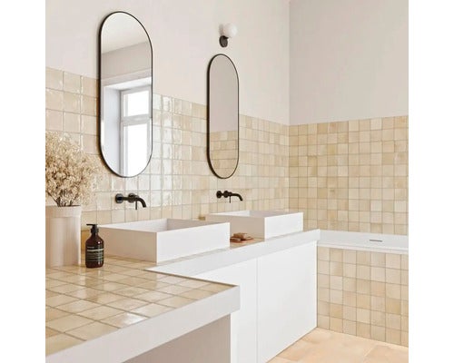 Modernes, helles Badezimmer mit beigen Wandfliesen, zwei weißen Aufsatzwaschbecken, ovalen Spiegeln und schwarzen Armaturen.