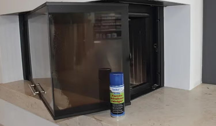 Sprühdose beko Kaminscheibenreiniger vor einem modernen Kamin mit Glasscheibe auf einem hellen Kaminsims.