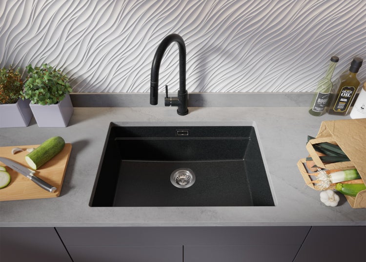 Schwarzes Spülbecken mit Armatur in einer modernen Küche mit Gemüse und Kräutern.