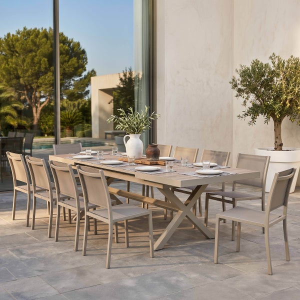 Modernes Gartenmöbel-Set auf einer Steinterrasse mit großem Esstisch mit X-Beinen und passenden Gartenstühlen in hellem Design.