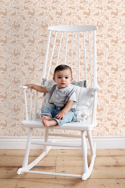 Baby sitzt in einem weißen Schaukelstuhl vor einer Tapete mit Tiermotiven.