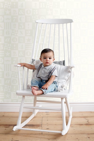 Ein Baby sitzt auf einem weißen Schaukelstuhl mit Kissen.