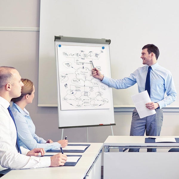 Mann hält eine Präsentation an einem Flipchart mit Papierblock in einem hellen Besprechungsraum.