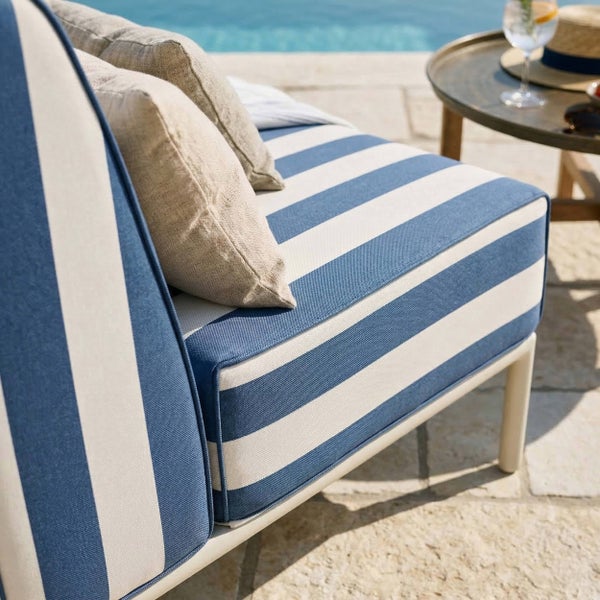 Gartenlounge mit blau und weiß gestreiften Polstern und beigen Zierkissen auf einer Terrasse am Pool.