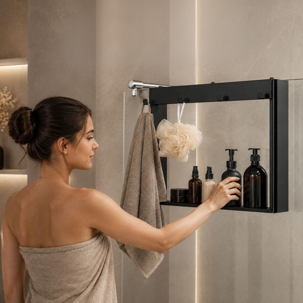 Frau in einem modernen Badezimmer, die eine schwarze Duschablage zum Aufhängen an einer Glaswand mit Pflegeprodukten und einem Handtuch benutzt.