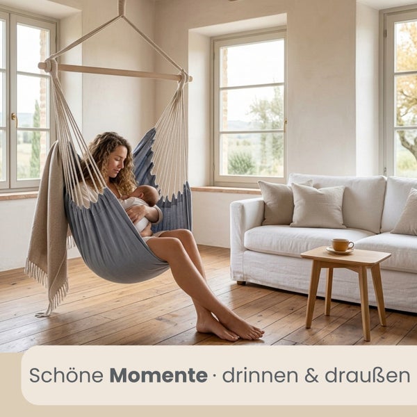 Frau mit Baby in einem hellblauen Hängesessel in einem hellen Wohnzimmer mit Parkett, weißem Sofa und kleinen Holzmöbeln.