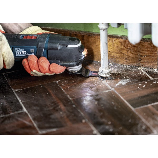 Multifunktionswerkzeug im Einsatz zum Schneiden von Holz neben einem Heizungsrohr