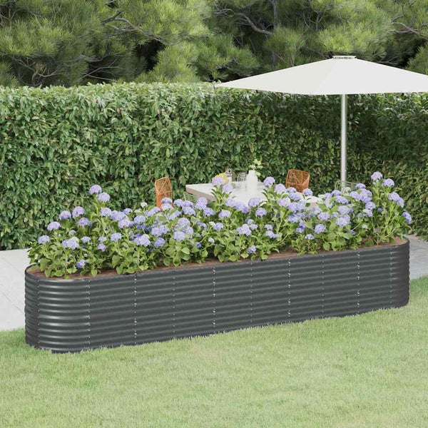 Längliches Hochbeet aus gewelltem Metall bepflanzt mit blauen Hortensien im Garten vor einer Hecke mit Gartenmöbeln im Hintergrund.