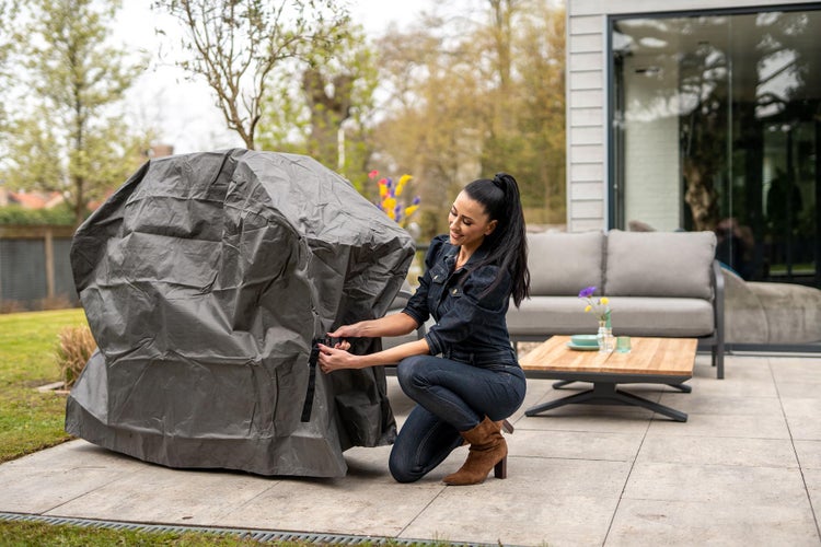 Frau befestigt eine graue Grillabdeckung auf einer Terrasse
