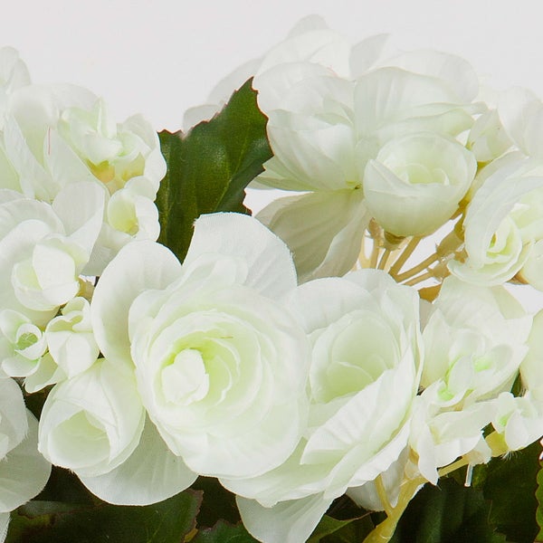 Nahaufnahme von künstlichen grünen Blättern mit gezackten Rändern und einer weißen Blüte in einem Pflanzgefäß.