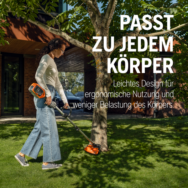 Eine Frau trimmt mit einem leichten Akku-Rasentrimmer Rasenkanten an einem Baumstamm im Garten.