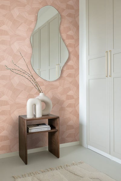 Vliestapete mit geometrischem Muster in einem modern eingerichteten Raum mit asymmetrischem Spiegel, Holztisch und Schrank.