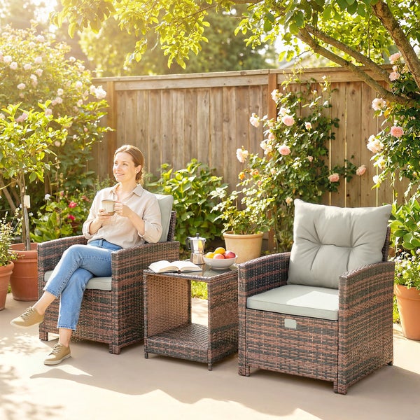 Frau in einem Garten-Set aus Polyrattan mit zwei Sesseln und Beistelltisch vor einem Holzzaun und Rosenbüschen.