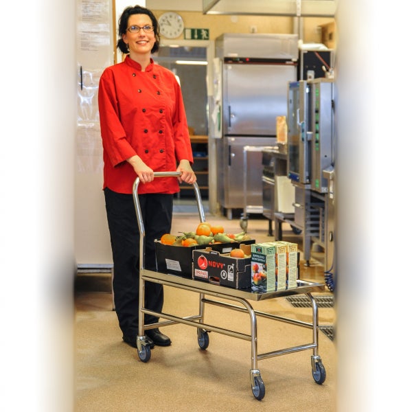 Frau in Kochkleidung schiebt Servierwagen mit Obst und Getränken in Großküche