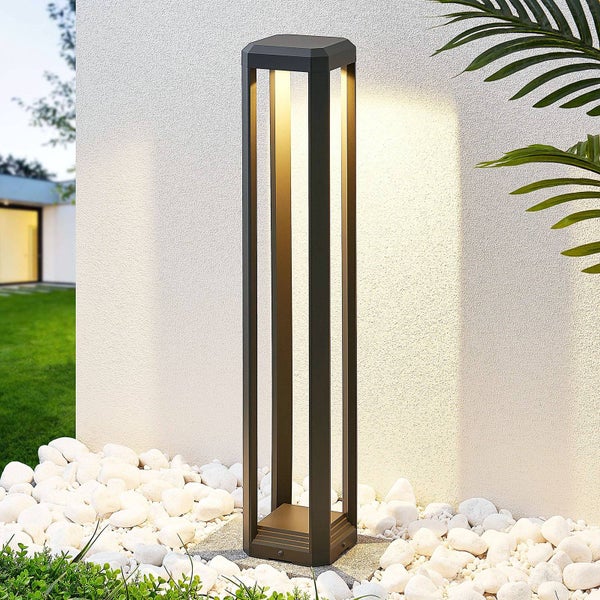 Moderne anthrazitfarbene Außenstandleuchte aus Metall mit LED-Licht, stehend in Kieselsteinen vor einer Wand.