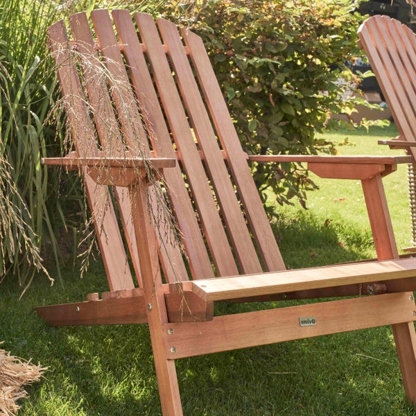 Adirondack-Gartenstuhl aus Holz in einem hellen Garten mit Rasen, Ziergräsern und Sträuchern.