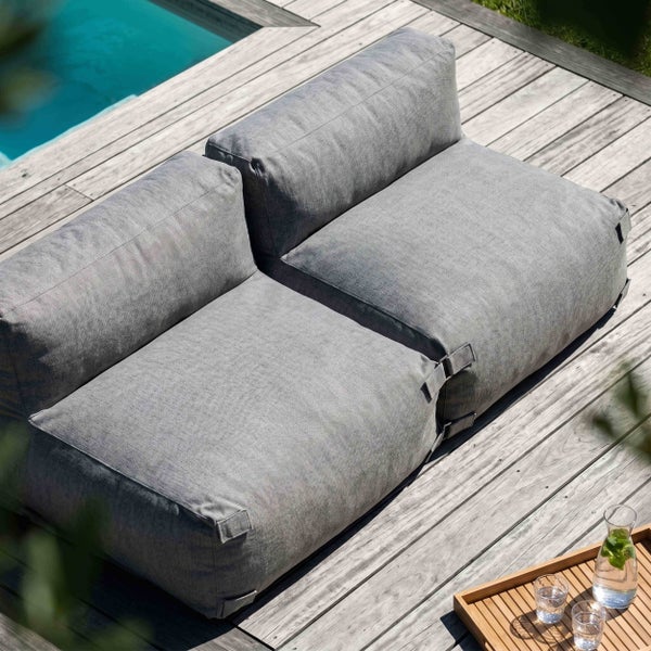 Modernes zweisitziges Outdoor-Sitzsack-Sofa in Grau auf einer Holzterrasse neben einem Pool.