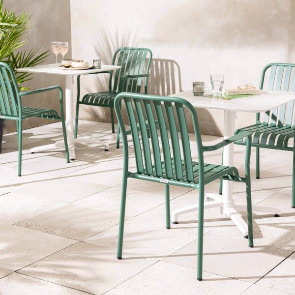 Helle Außenszene mit modernen grünen Metall-Gartenstühlen und weißen quadratischen Bistrotischen auf einer Steinterrasse.