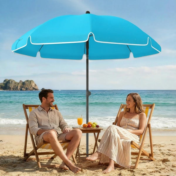 Ein Mann und eine Frau sitzen entspannt in hölzernen Liegestühlen unter einem blauen Sonnenschirm an einem hellen Strand am Meer.