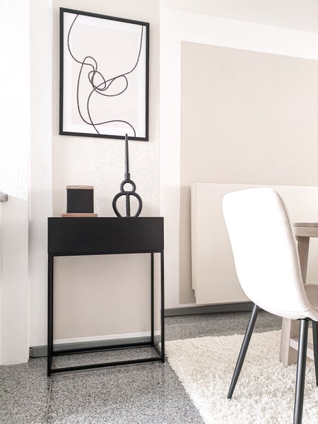Modernes, minimalistisches Zimmer mit schwarzem Konsolentisch, abstrakter Wandkunst und hellem Stuhl auf einem Hochflor-Teppich.