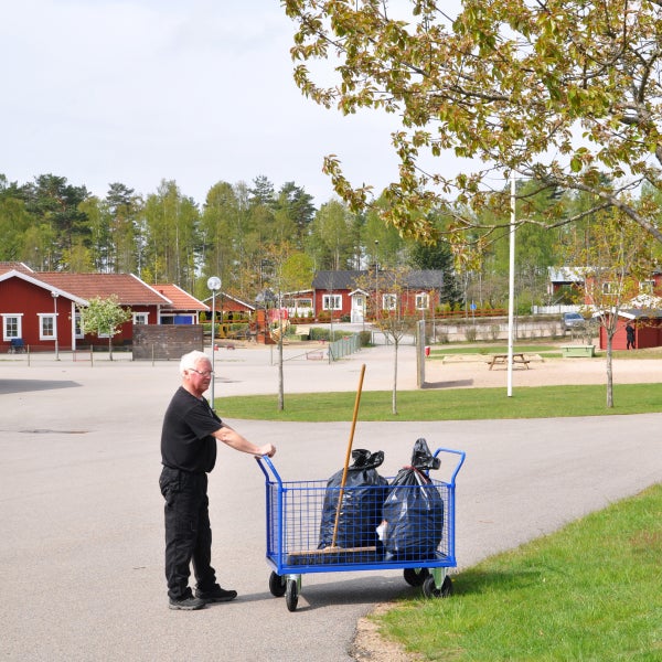 Eine Person schiebt einen blauen Gitterwagen mit Müllsäcken und Reinigungsutensilien.