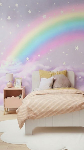Kinderschlafzimmer mit Wandbild mit Regenbogen, Sternen und Wolken, weißem Holzbett, gestreifter Bettwäsche und wolkenförmigem Teppich.