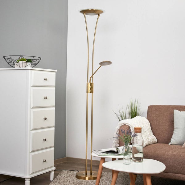 Goldfarbene Stehleuchte mit Deckenfluter und Lesearm aus Metall und Glas in einem hellen Raum neben einer weißen Kommode.