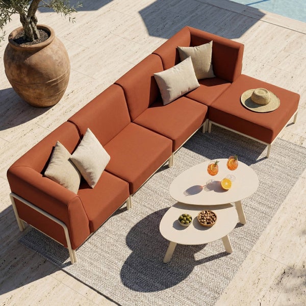 Moderne Outdoor-Ecklounge mit ovalen Tischen, Teppich und Terrakotta-Pflanzgefäß auf einer Steinterrasse.